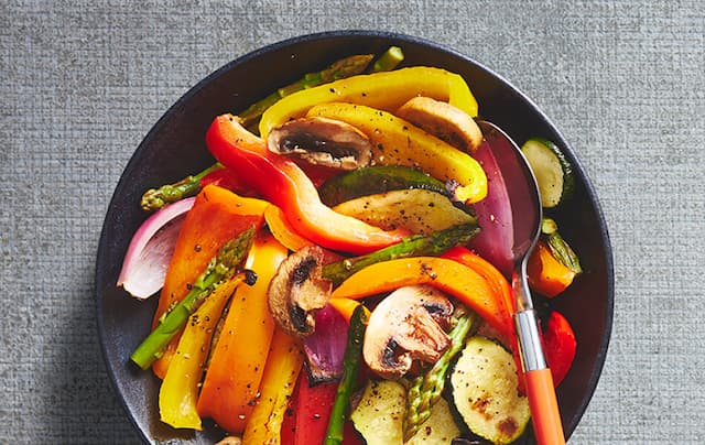 Deluxe mixed vegetable griller in a black bowl with an orange handled spoon
